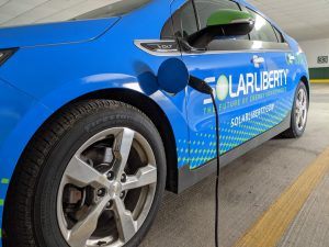 Blue sedan with "Solar Liberty" wrap text, hooked up to EV charger in parking garage