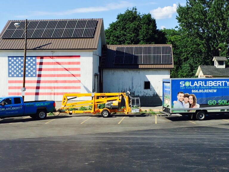 Solar liberty truck parked in front of small building with solar panels on roof and American flag on side